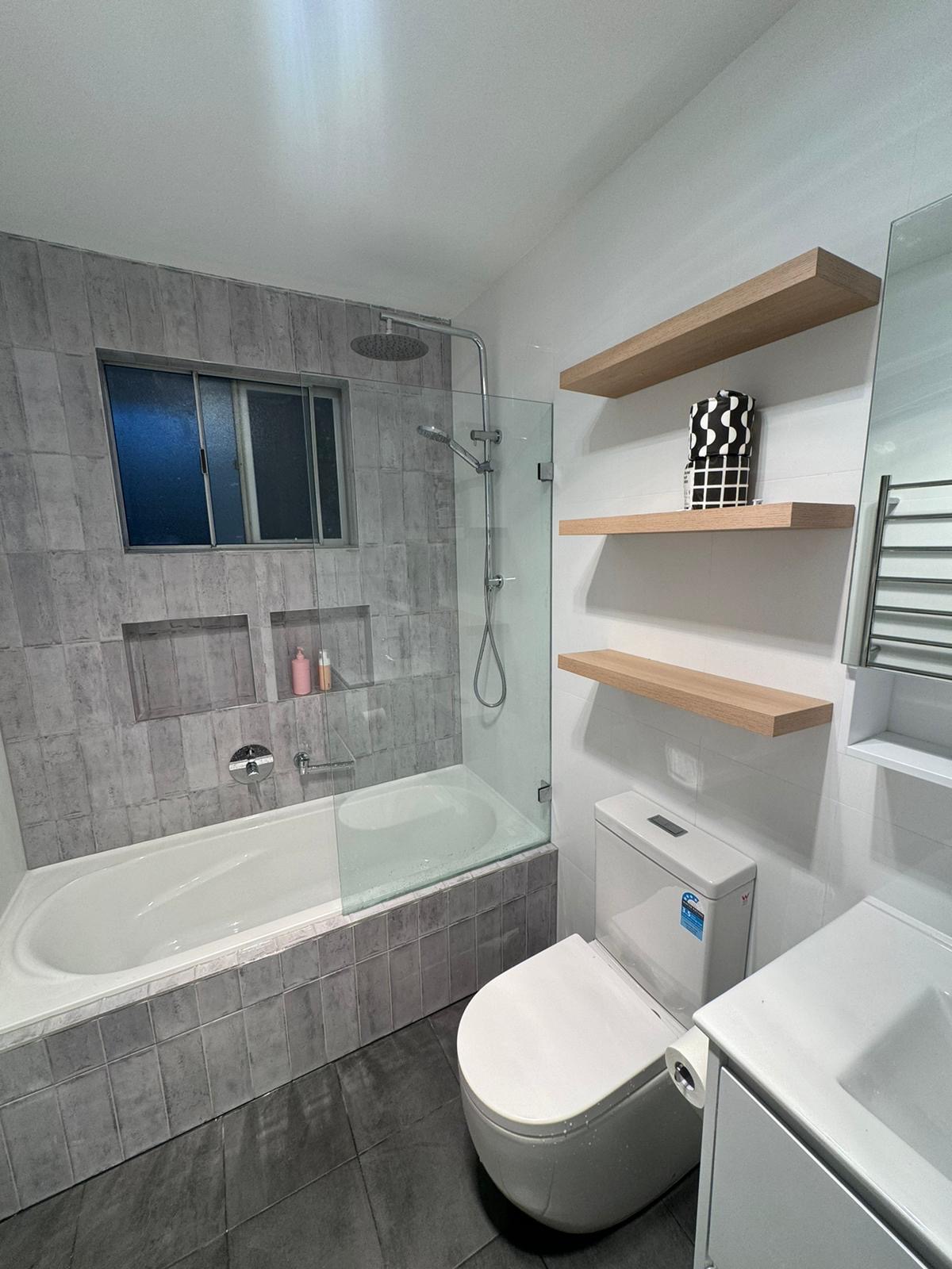 Family bathroom with grey tiles, bath and floating shelves