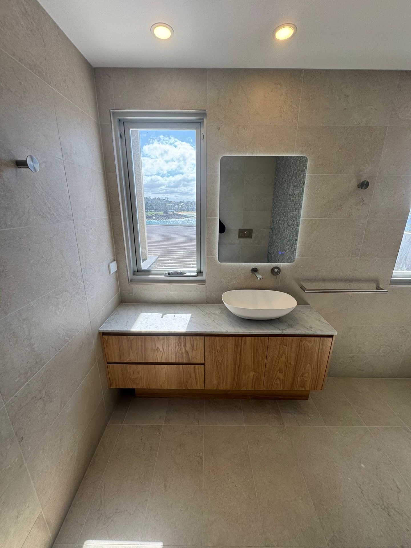 Stone-tiled bathroom with timber vanity and ocean view
